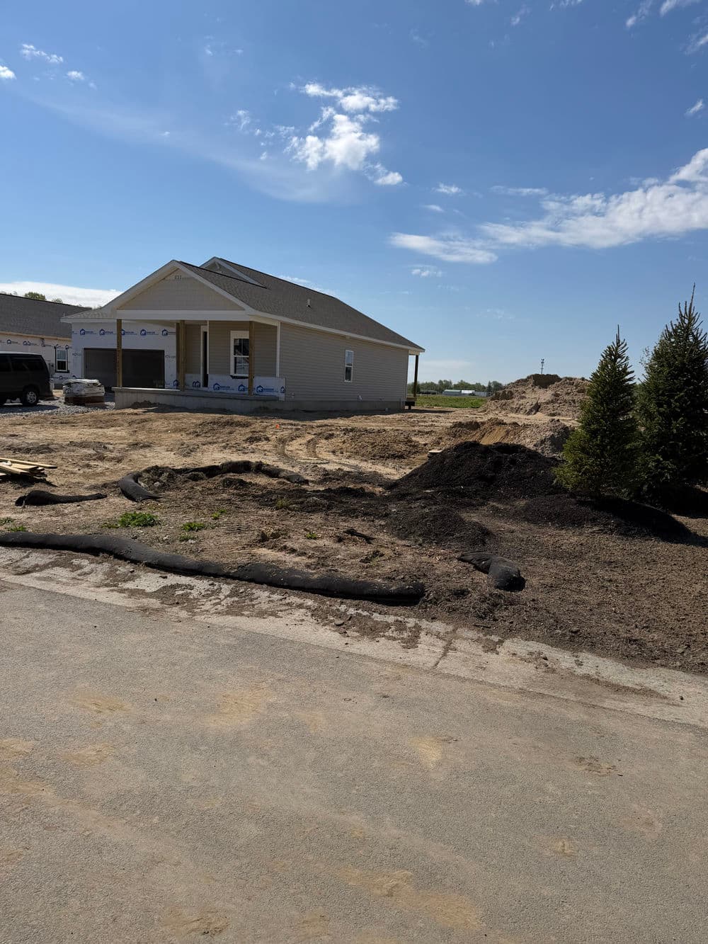 Newly constructed home with landscaping in progress, surrounded by dirt and trees.