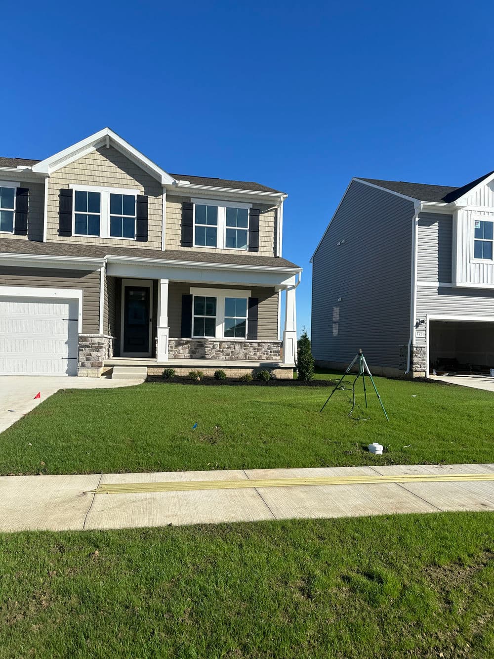 Newly constructed two-story house with front yard, modern design, and clear blue sky.