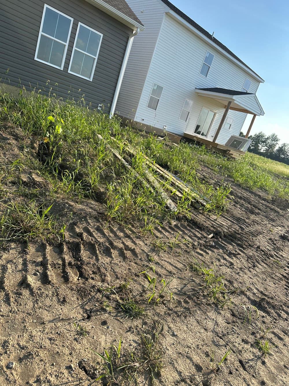 New construction home with overgrown grass and fresh dirt near the foundation, showcasing landscaping.