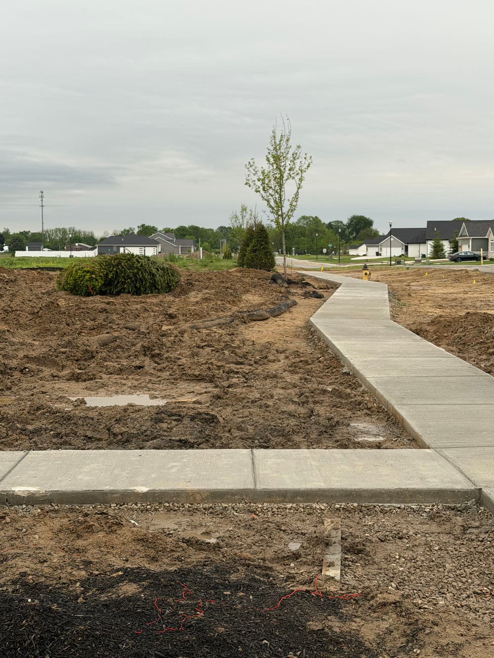 Construction site with newly paved sidewalk and landscaped areas under a cloudy sky.