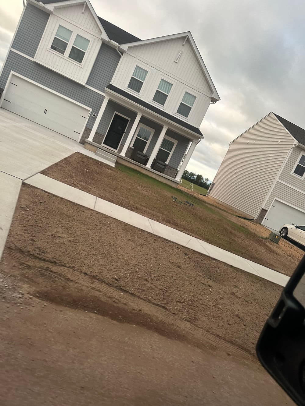 Two-story modern house with gray siding, porch chairs, and a plain front yard.