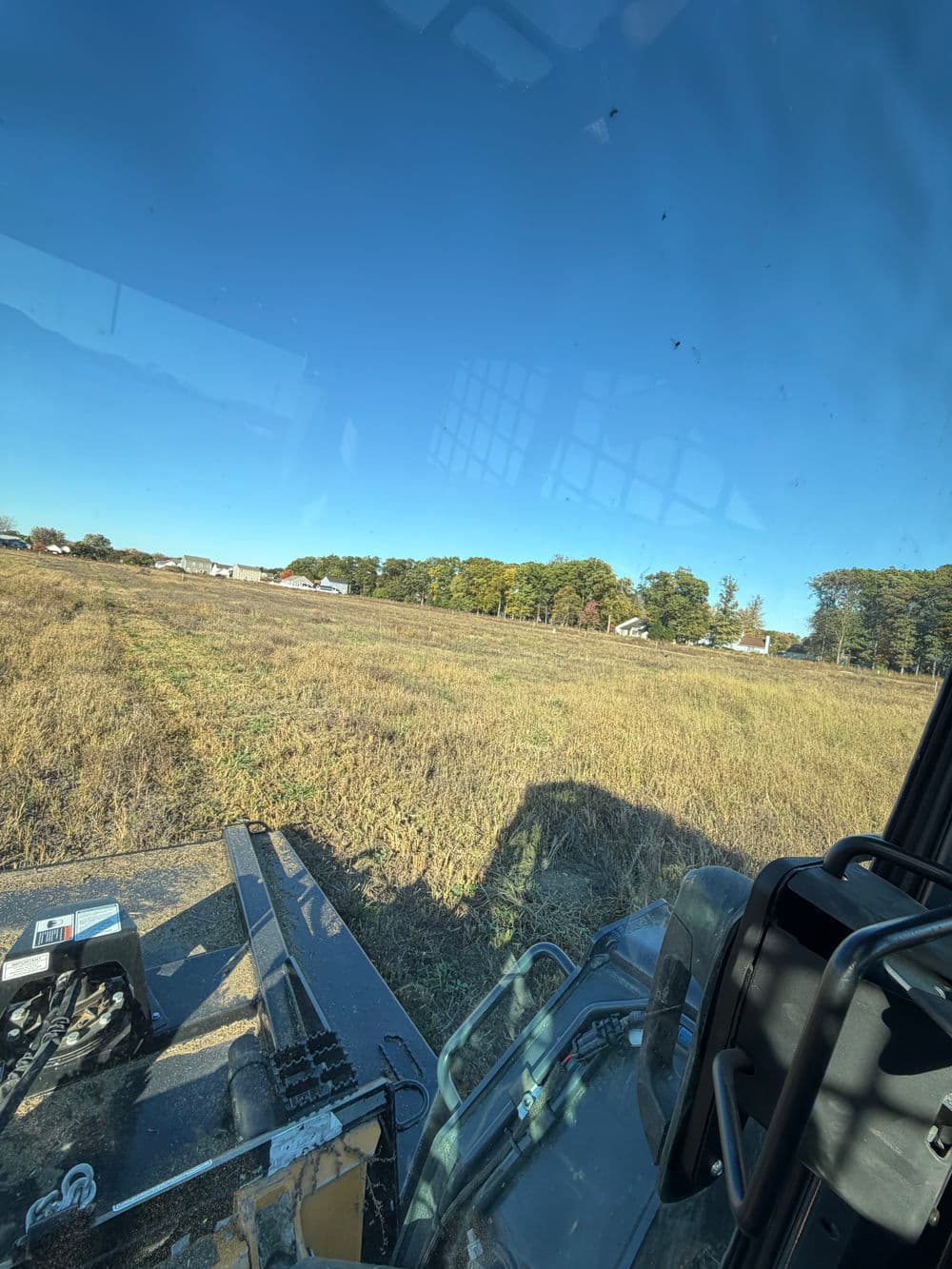 View from a tractor in a field under a clear blue sky, showcasing farmland and trees.
