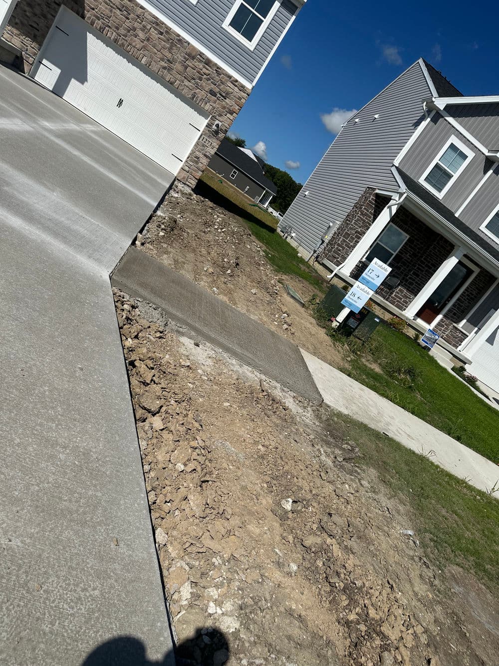 Newly poured concrete driveway with freshly graded landscaping near residential homes.