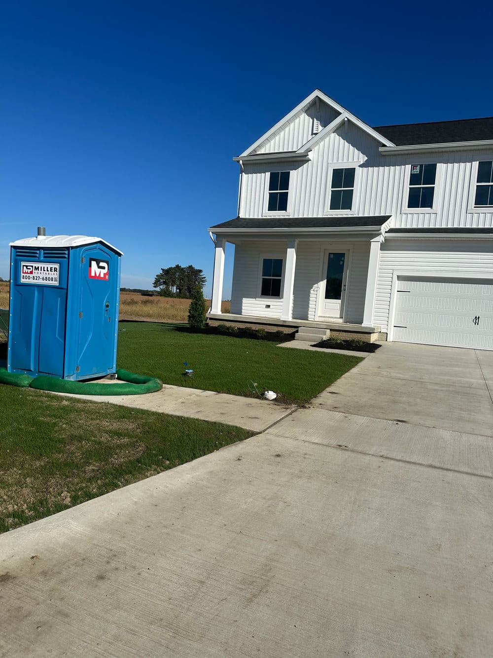 New construction home with a portable toilet on the lawn under a clear blue sky.