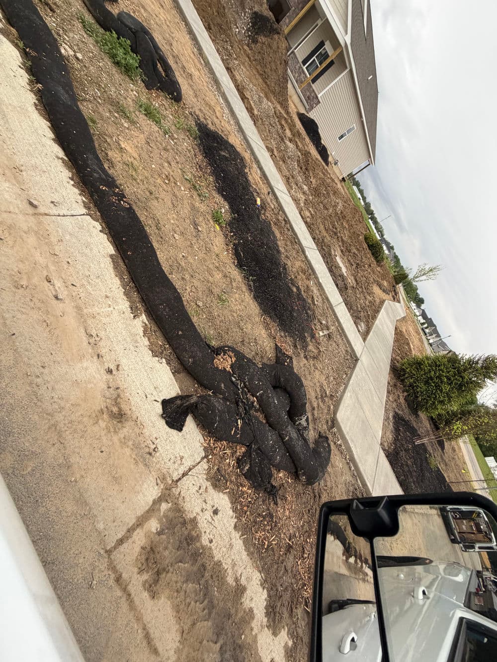 Curved black landscaping fabric on bare soil near a new construction home.