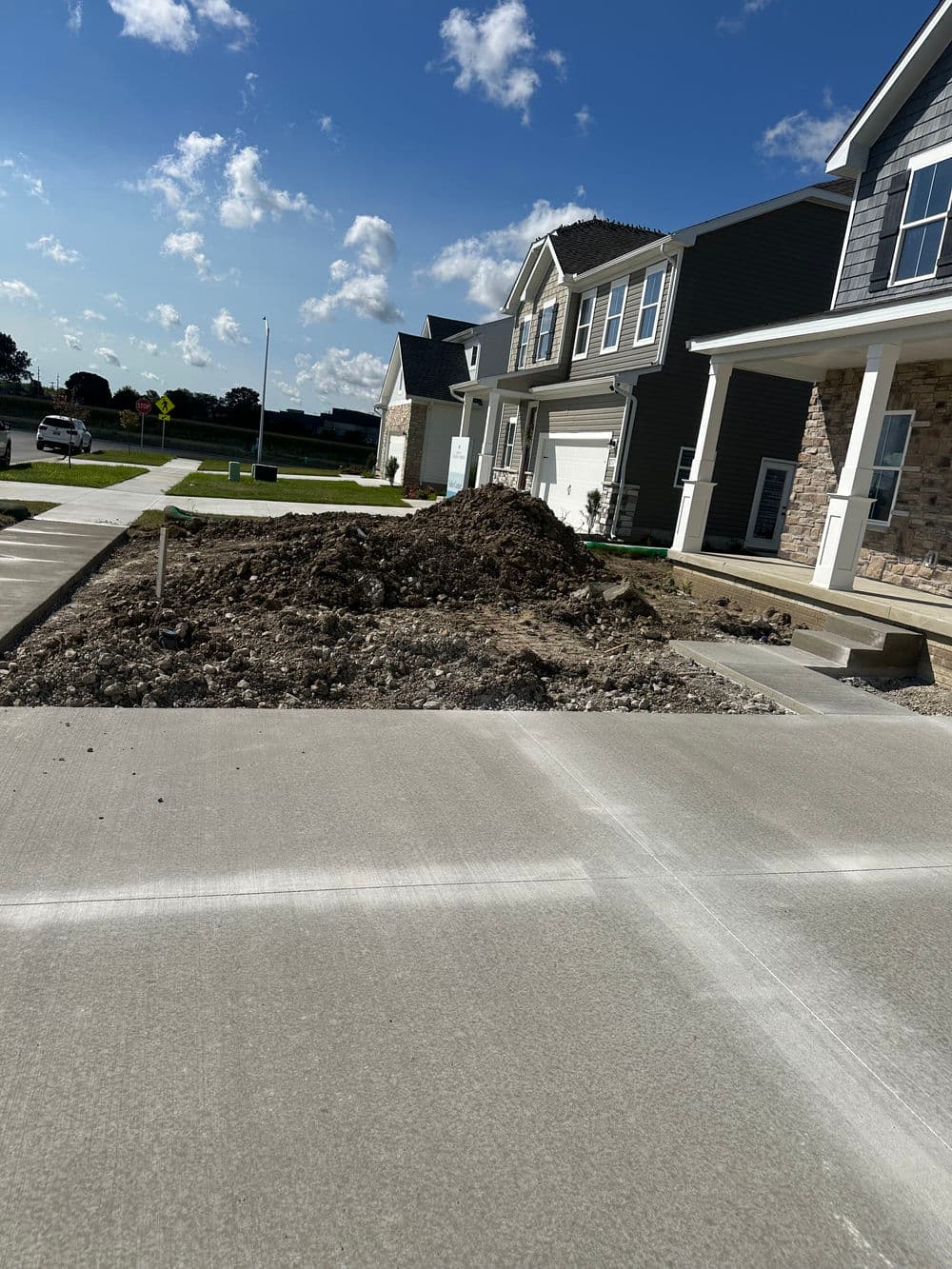 Residential construction site with dirt pile and newly poured concrete driveway.