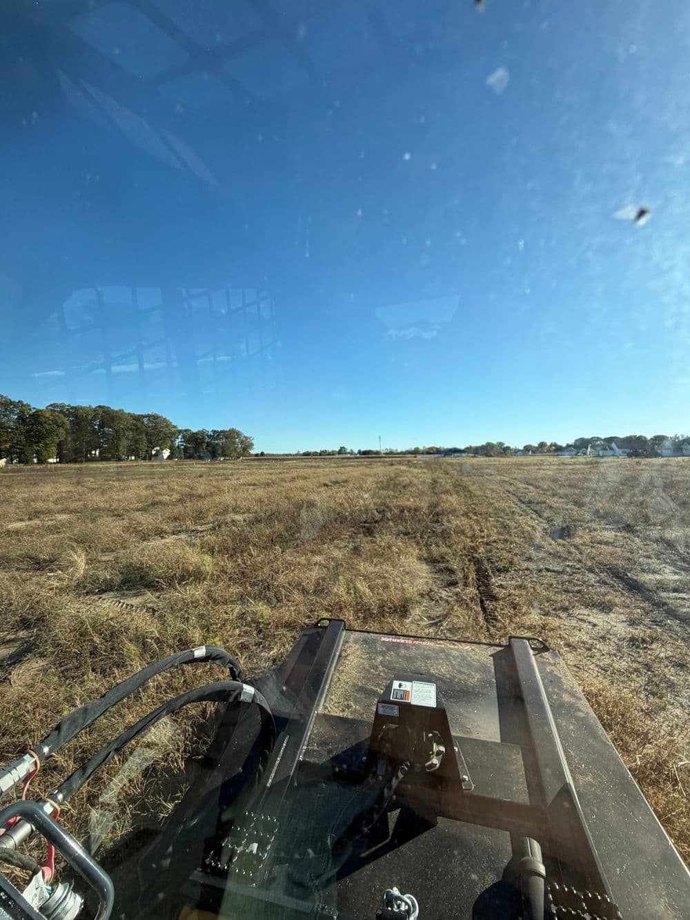 View from a tractor driving across a grassy field under a clear blue sky.