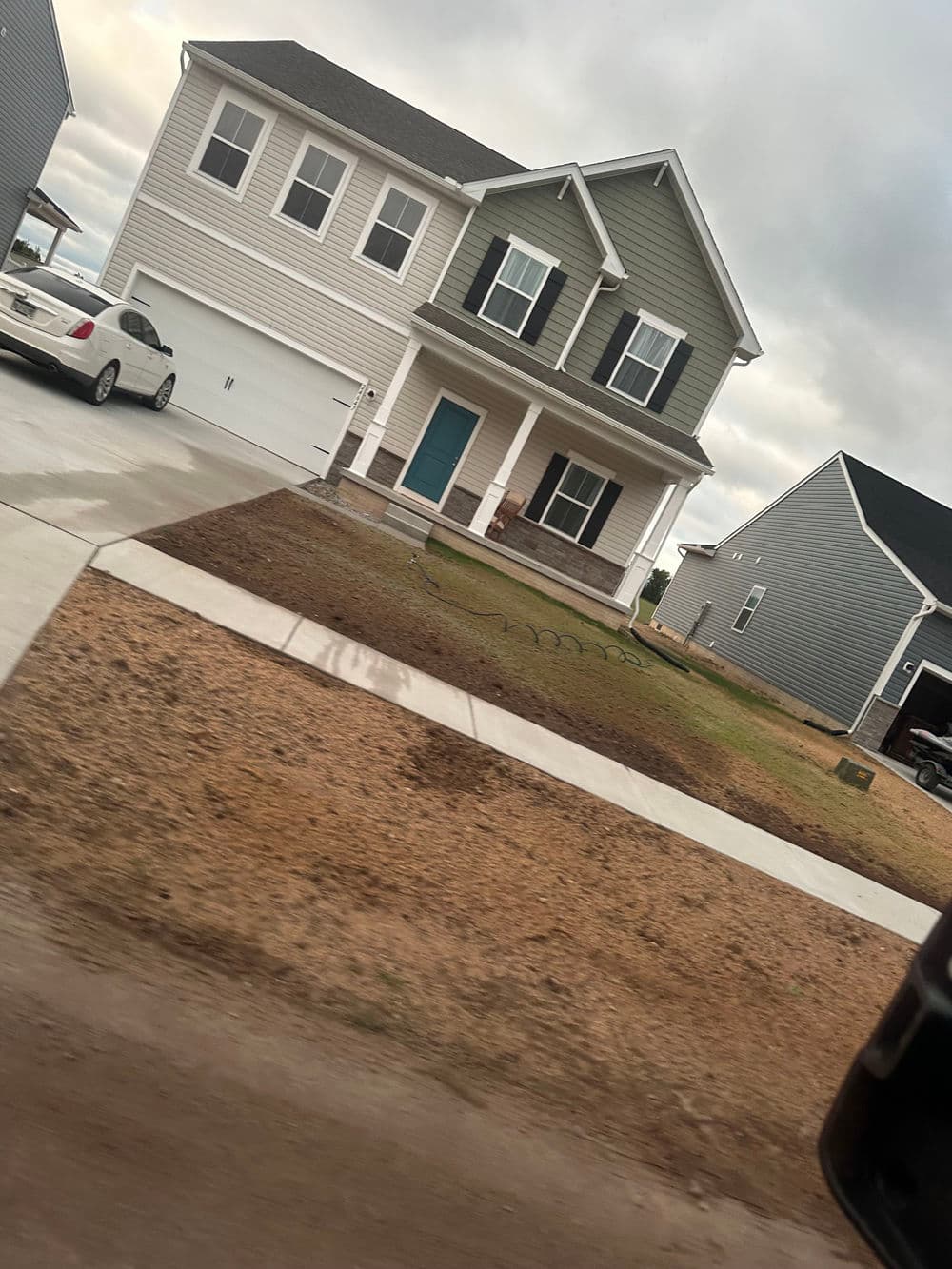 Modern two-story house with a green and gray exterior, driveway, and lawn.