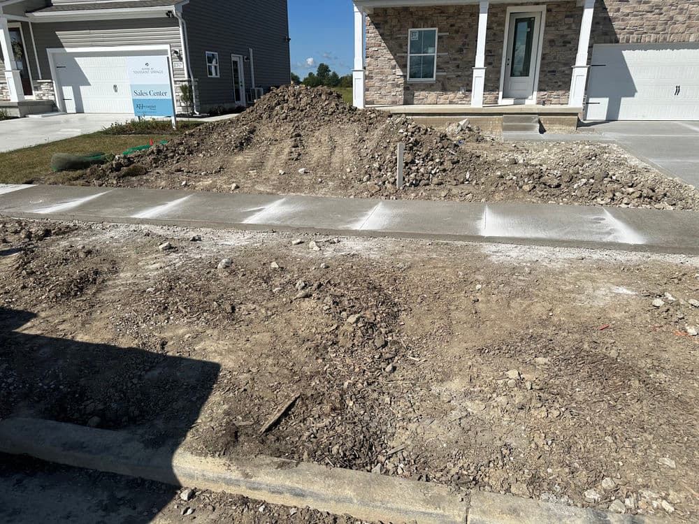 Newly poured concrete sidewalk beside a construction site with dirt and gravel.