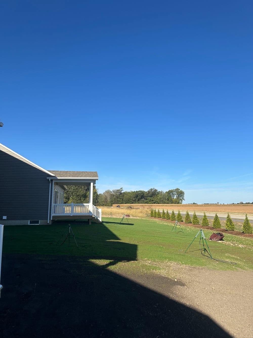 View of a home exterior with a clear blue sky and landscaped yard in a rural setting.