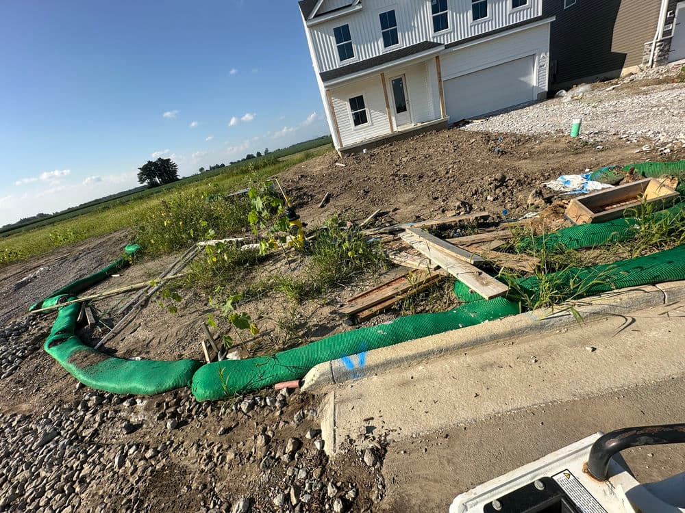 Construction site with green silt fencing, debris, and a new house in progress.
