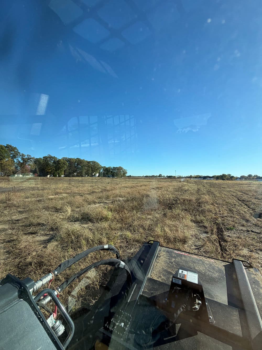 View from a tractor cabin overlooking a grassy field on a clear day.