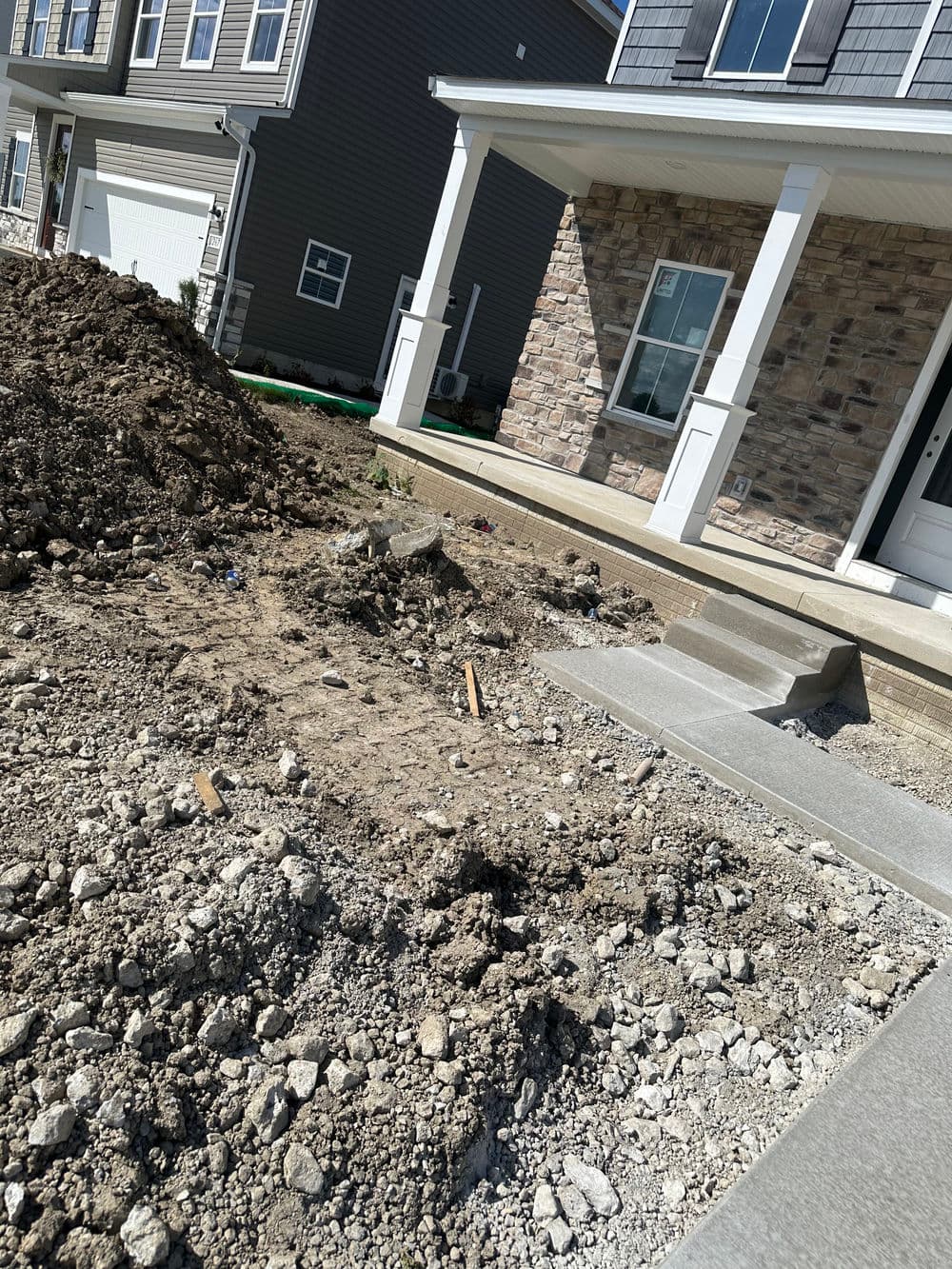 Construction site with dirt mounds and gravel near a residential home entrance.