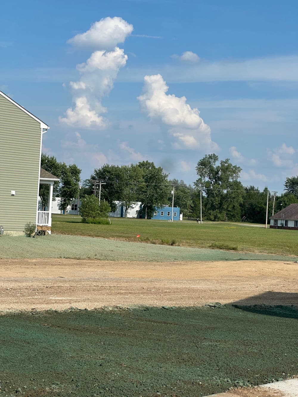 View of a rural landscape with blue sky, clouds, and green fields near houses.