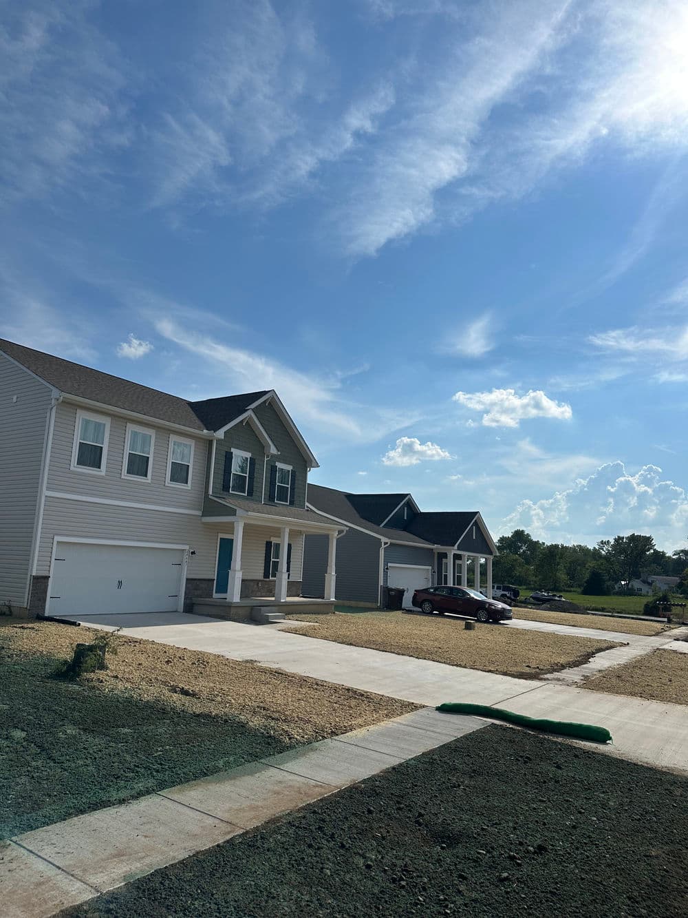 Newly built homes with driveways under a blue sky and scattered clouds.