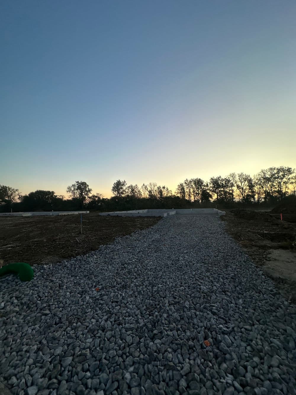 Gravel pathway leading through a construction site at sunset with trees in the background.