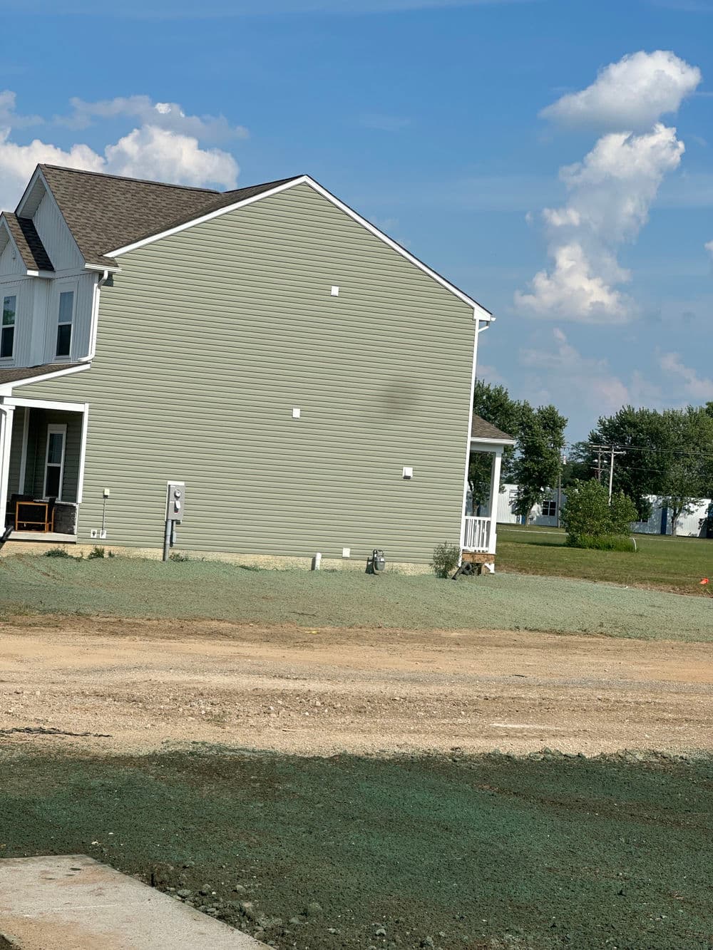 New residential home exterior with green siding and clear blue sky. Ground with gravel.