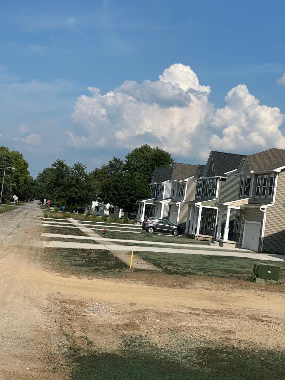 New residential neighborhood with house fronts and blue sky, featuring clouds.