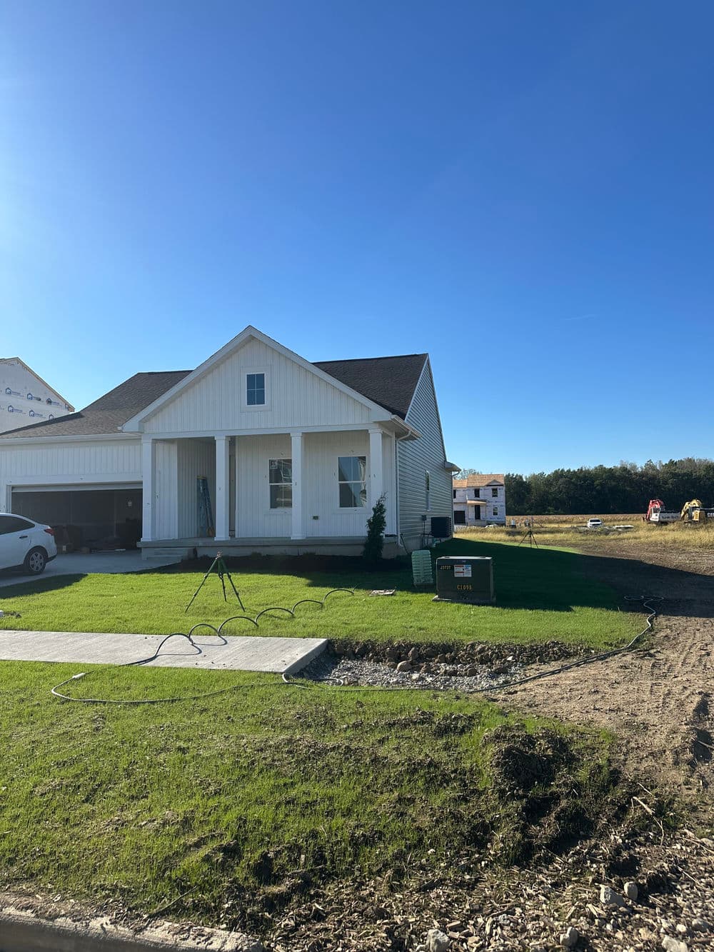 Newly constructed white house with green lawn and driveway under clear blue sky.
